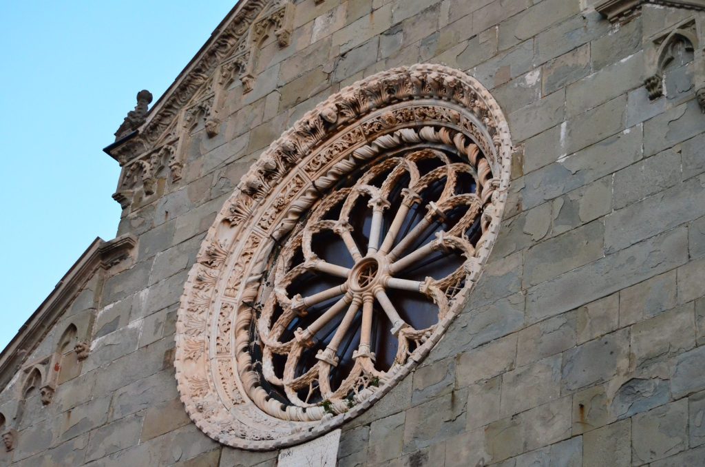 Histórica fachada de iglesia de piedra que presenta un gran rosetón circular con intrincada tracería radial y detalles decorativos tallados contra un cielo azul despejado.