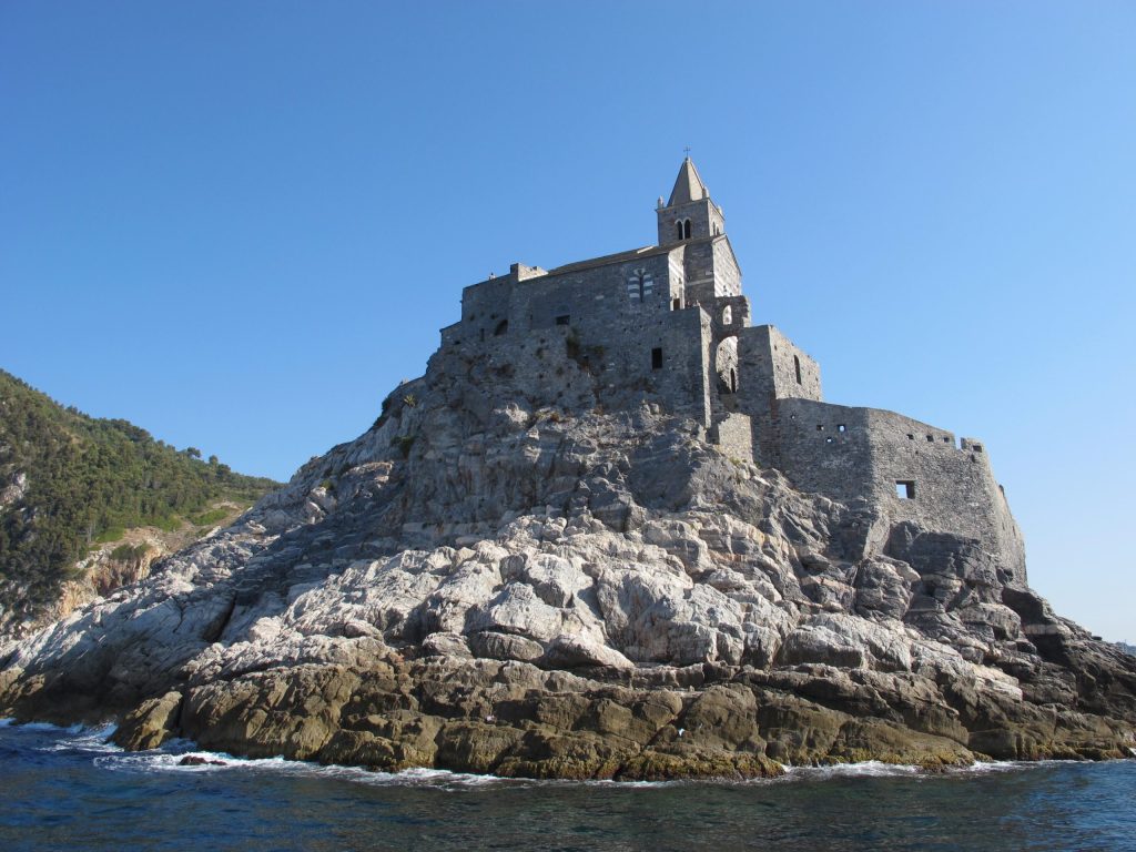 Castello di San Pietro a Porto Venere arroccato su un promontorio roccioso con mura in pietra grigia, affacciato sul mare blu sotto un cielo limpido, classica fortezza costiera ligure