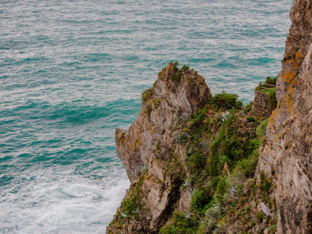 Los acantilados costeros de Manarola dominan el mar de Liguria de color turquesa, con bordes rocosos escarpados con vegetación verde y flora costera a lo largo de la costa mediterránea