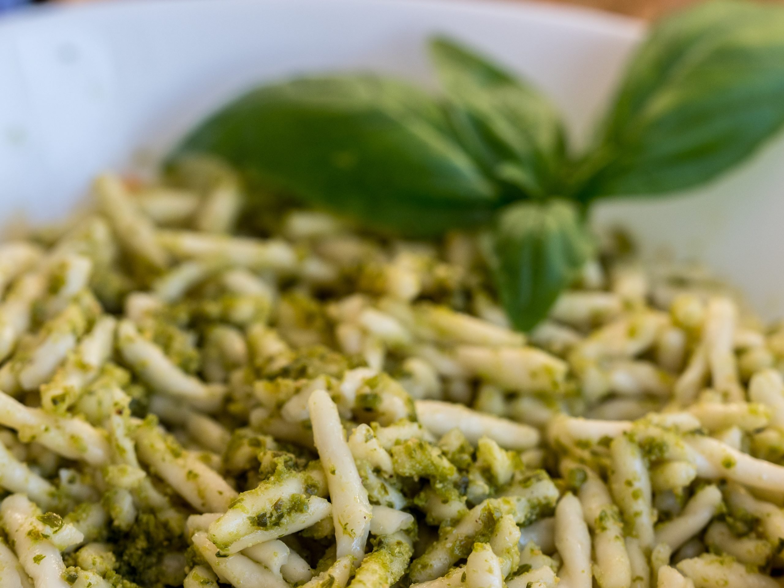 Primer plano de pasta con pesto de albahaca verde en un cuenco blanco: pasta en forma de espiral aderezada con pesto de hierbas y una hoja de albahaca fresca, ideal para una comida «Cinque Terre Riviera».
