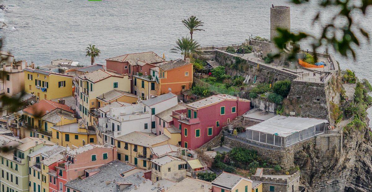 Colorido pueblo costero italiano con casas en tonos pastel situadas en un promontorio rocoso sobre un pequeño puerto, captado en Cinque Terre Riviera junto a barcas y una pintoresca costa.