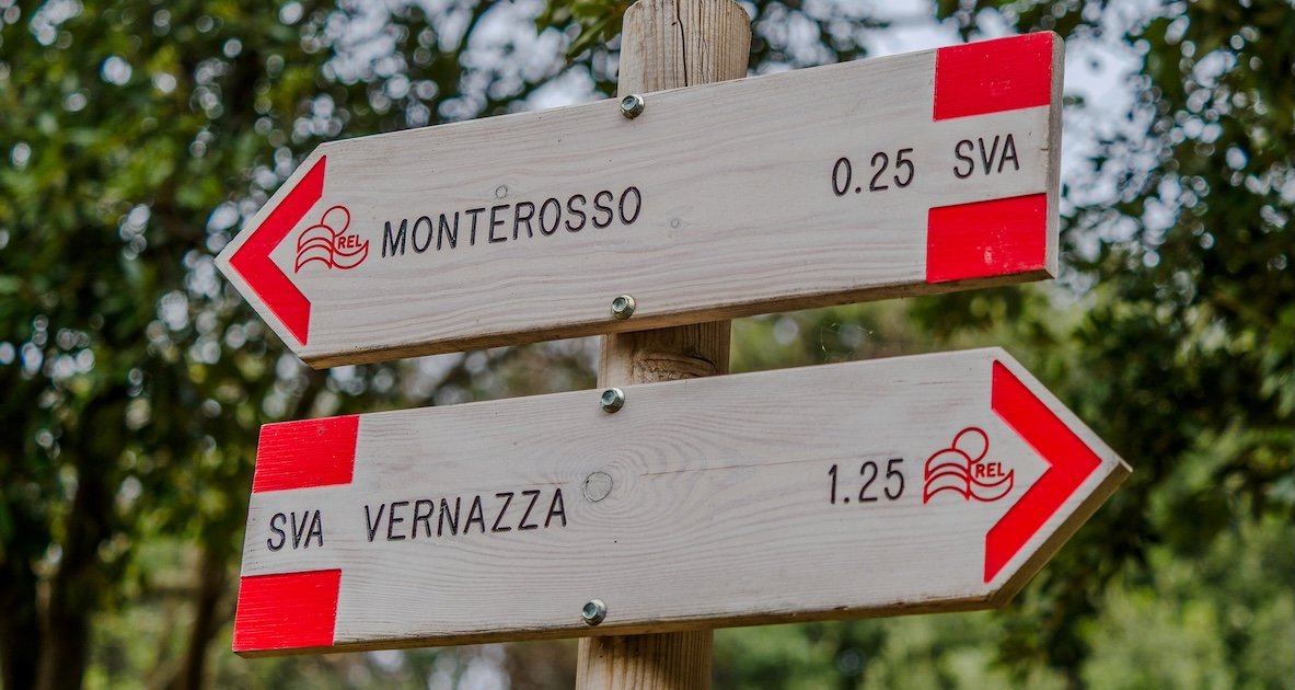 Señales indicadoras de madera con detalles en rojo en un entorno exterior, que apuntan hacia Monterosso y Vernazza a lo largo de los senderos de las Cinque Terre.