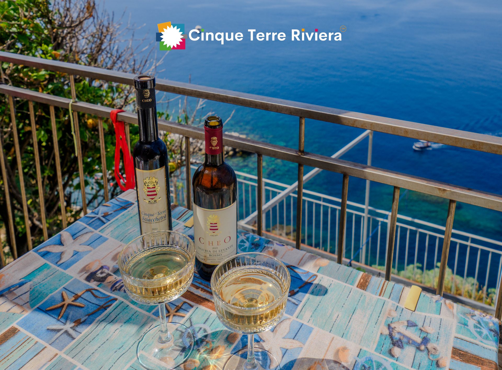 Dos copas de vino blanco local y botellas de vino de Cinque Terre en una mesa de terraza con vistas al mar