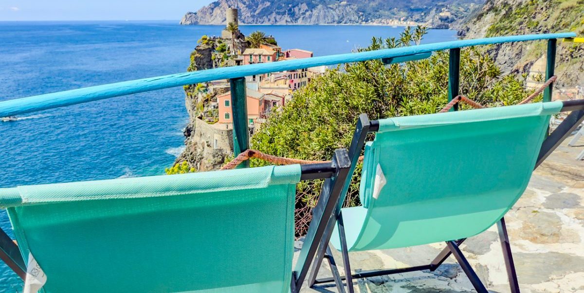 Tumbonas turquesas dominan Vernazza, la torre medieval de Muìn a Véntu y el azul del mar de Liguria con acantilados que se elevan más allá de las Cinque Terre.