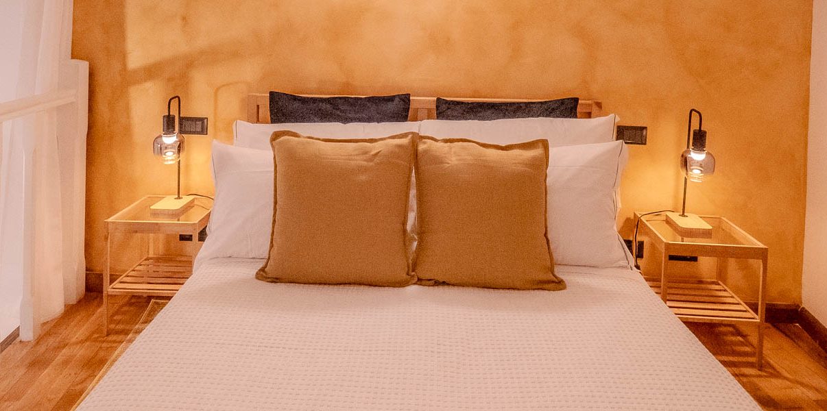 Dormitorio cálidamente iluminado en Petrella's Point en Vernazza, con una cama doble, cojines marrón claro, lámparas de noche y paredes de terracota en un estudio reformado en la planta baja.